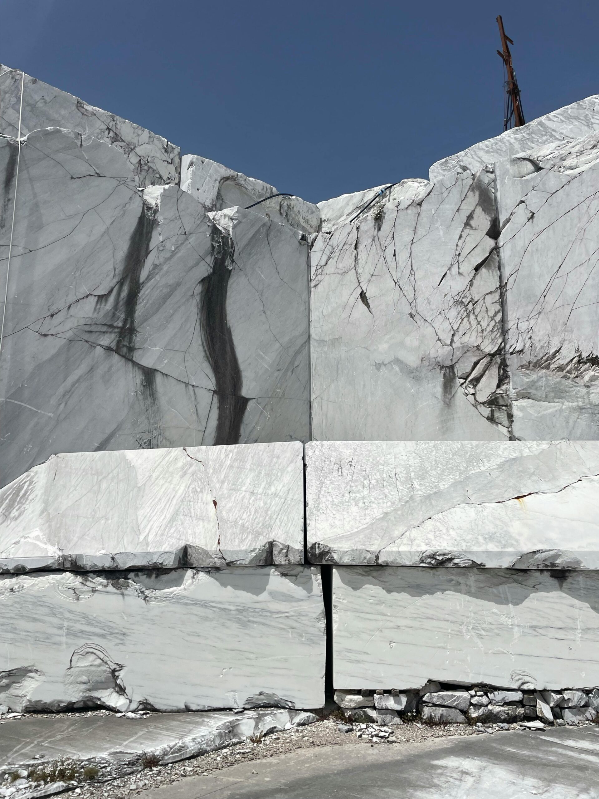 Products Large white marble blocks with cracks in an open quarry under clear blue sky.