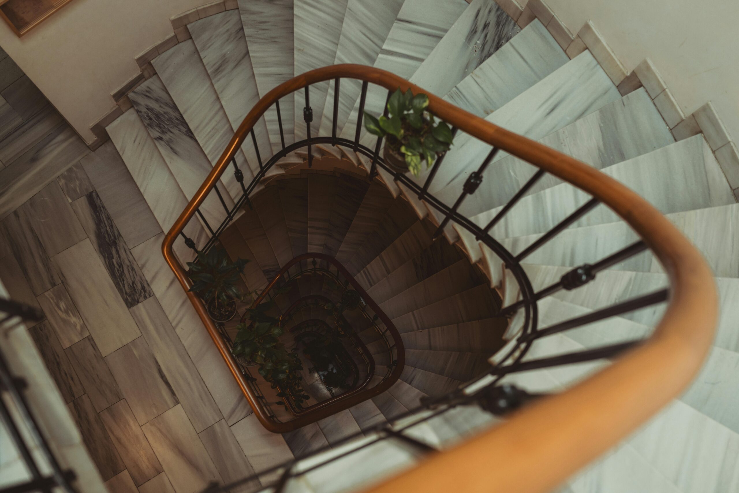 Products Elegant spiral staircase with plants and wooden handrail in marble interior. Aerial view.