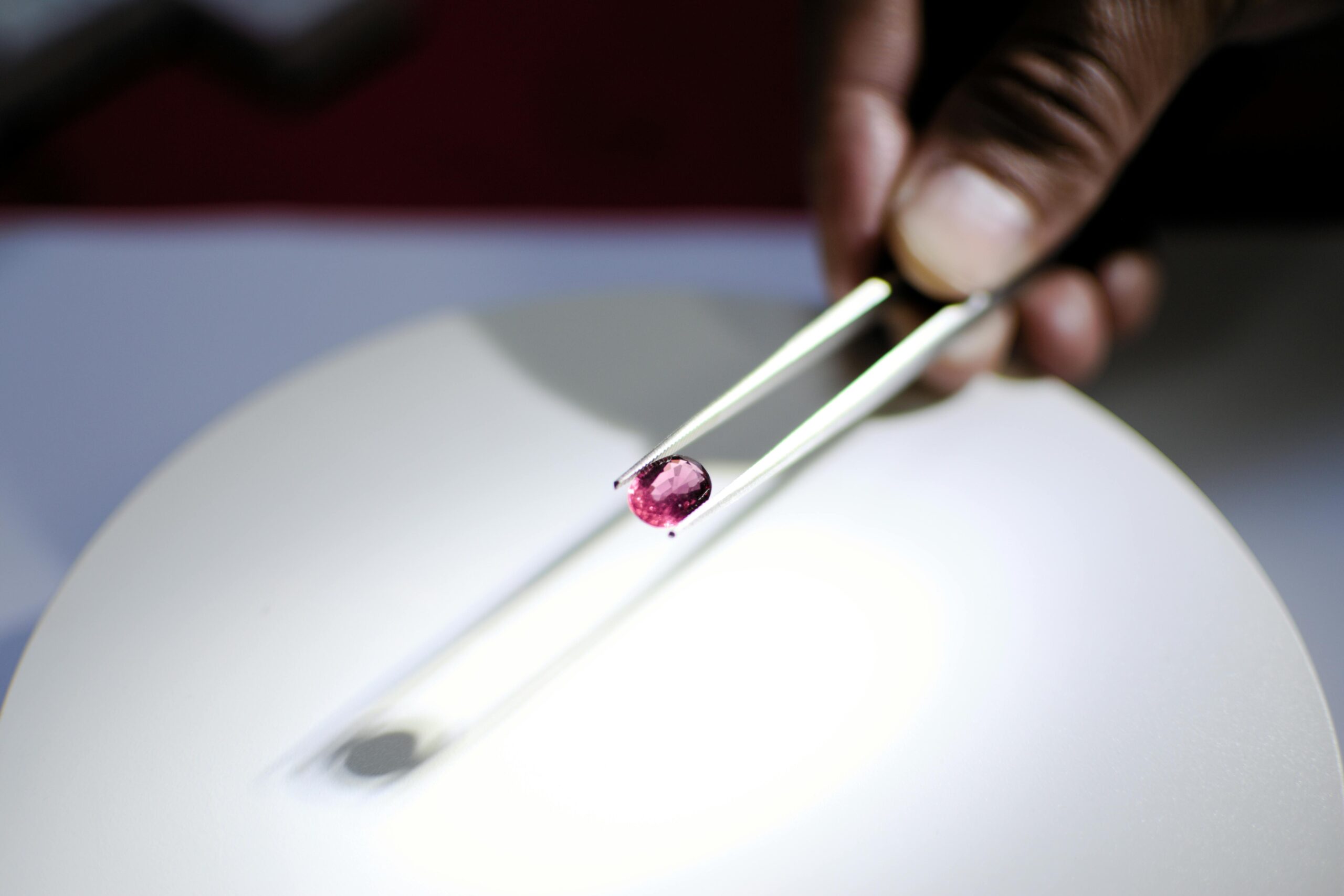 Products Detailed image of a hand holding a red gemstone using tweezers, perfect for jewelry and gemology themes.